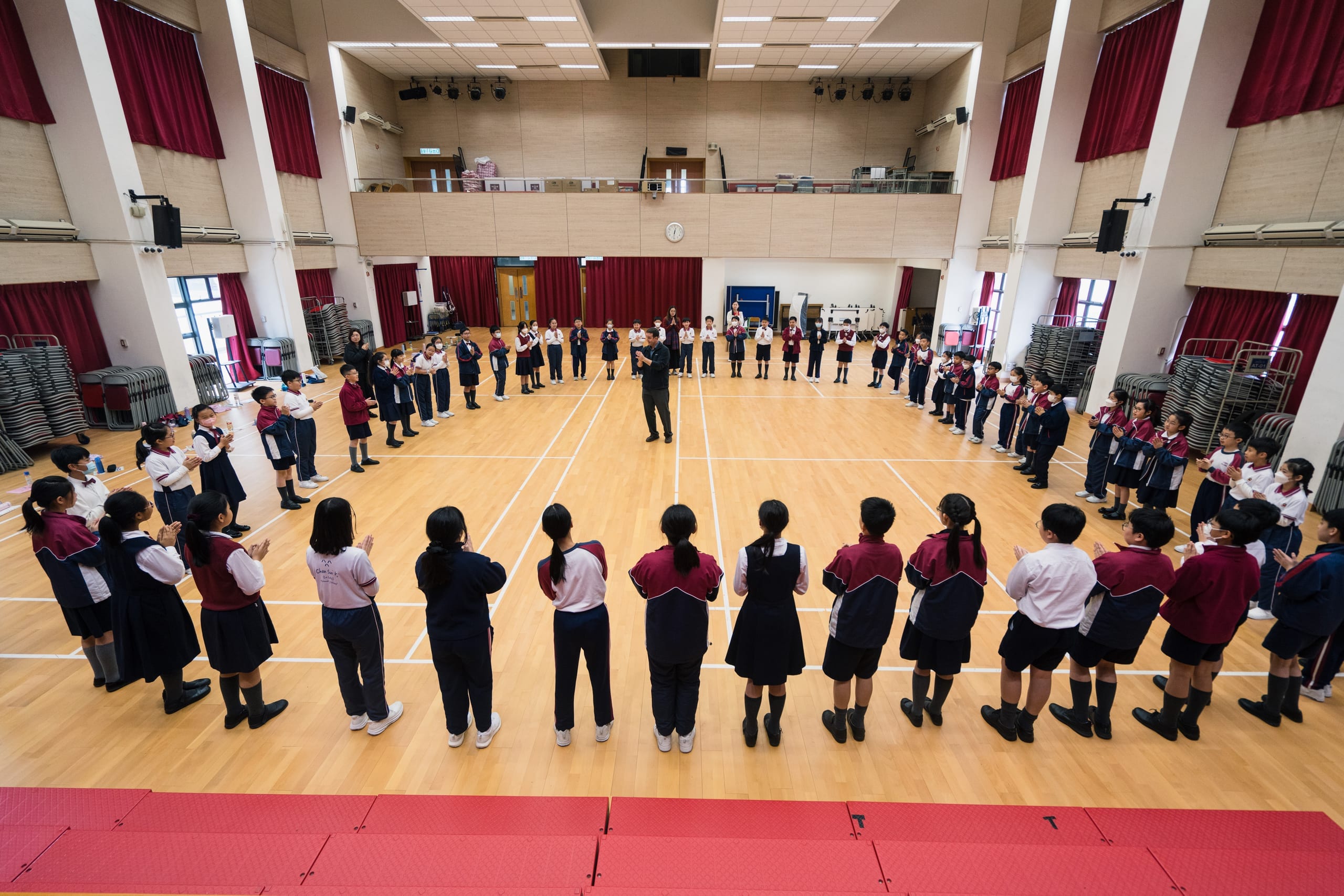 Students standing in a large circle around a conductor in a school hall during an HKVC choral workshop